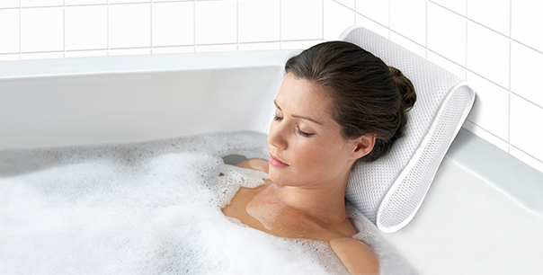 A very pretty woman is blisfully relaxing in a bathtub with her head comfortabley supported by an aerocore(tm) bathpillow